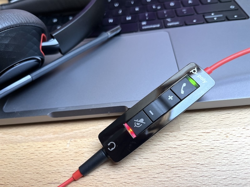 Picture of a headset and it's call control device where light indicators for active call and mute are on